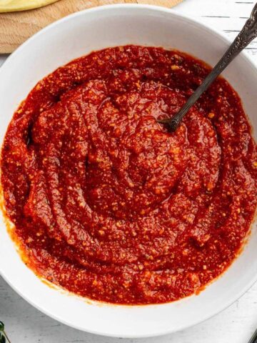 Overhead close up of pizza sauce in a white bowl with a spoon.