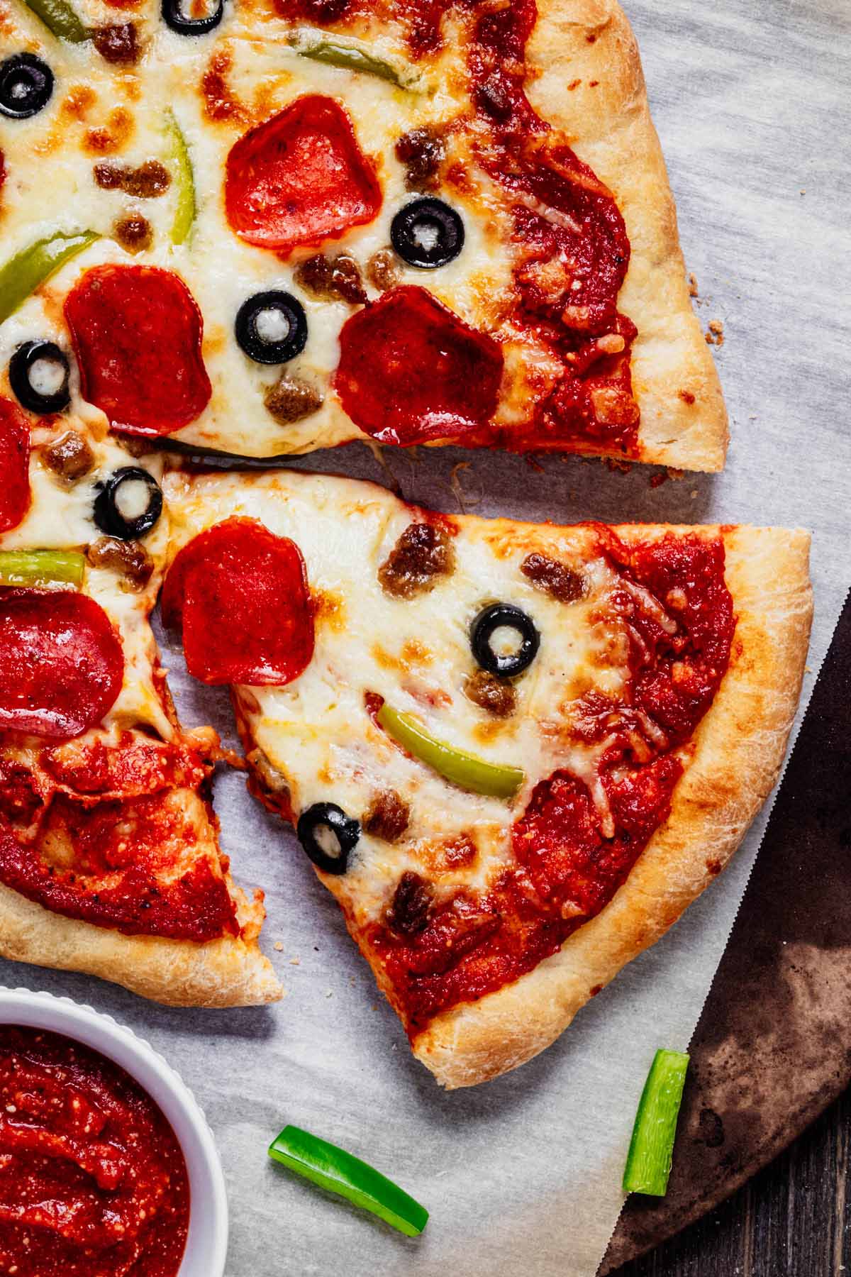 Overhead close up of homemade supreme pizza on parchment paper. A slice is pulled out.