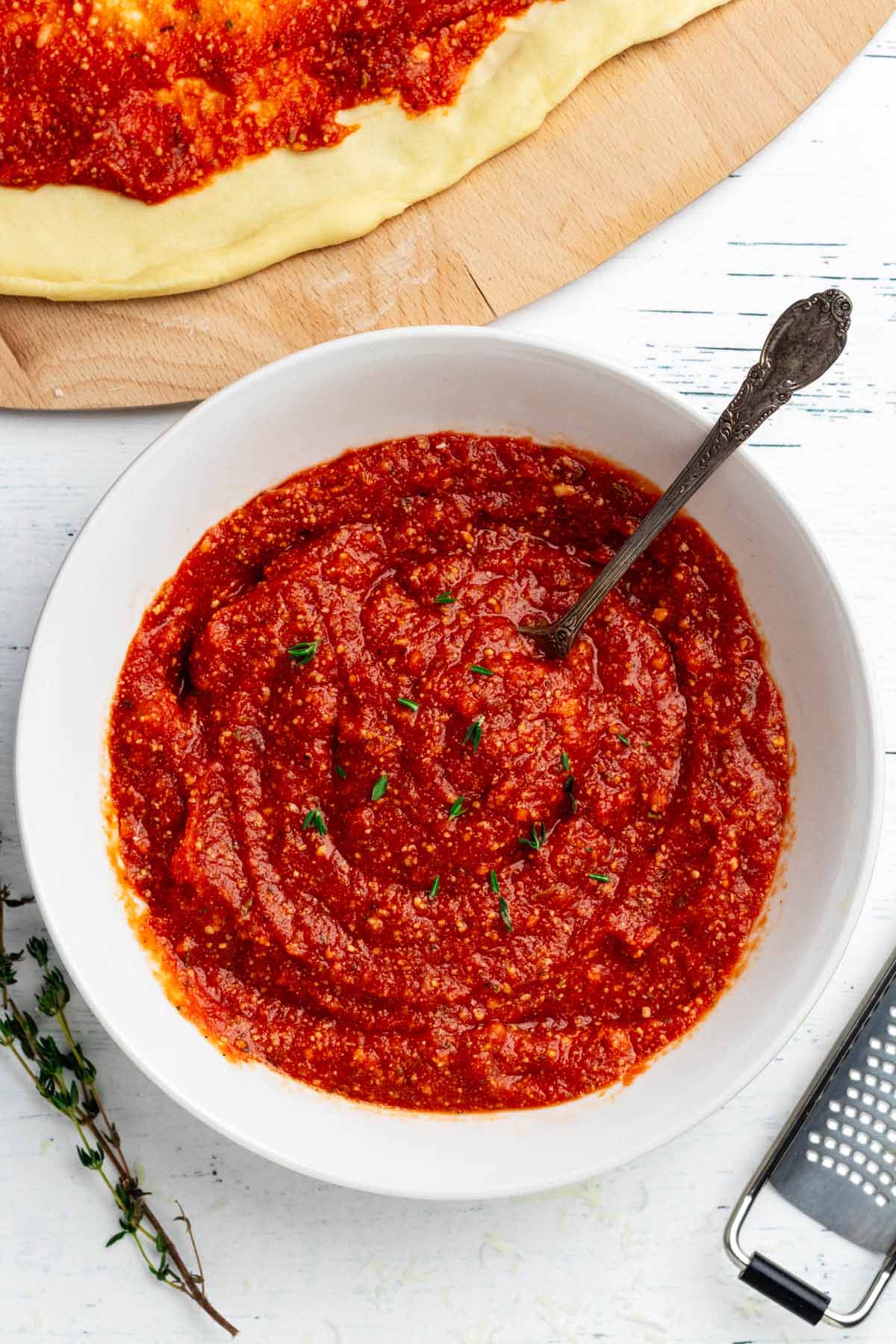 Overhead view of pizza sauce in a white bowl with a spoon.