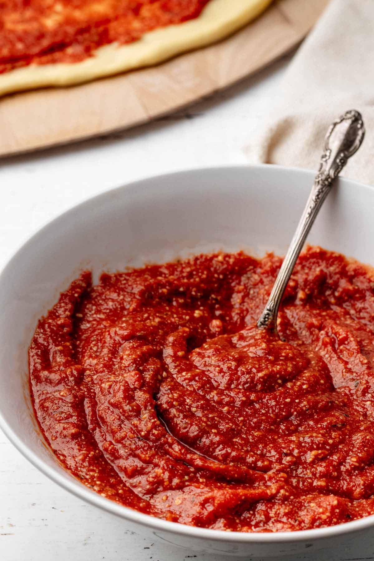Close up of homemade pizza sauce in a white bowl with a spoon.