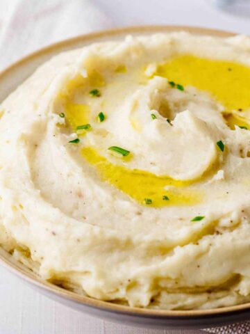 Close up of of truffle mashed potatoes garnished with olive oil and chopped chives in a light bowl with beige trim.