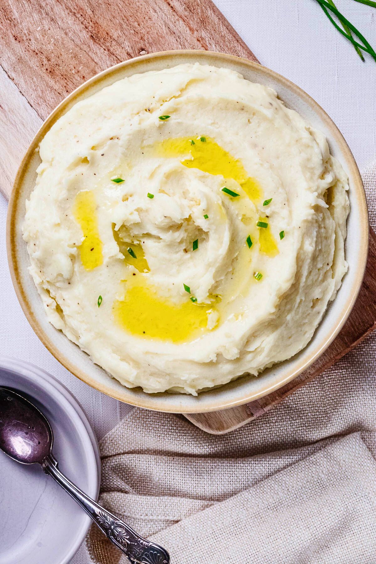 Overhead close up of truffle mashed potatoes garnished with olive oil and chopped chives in a light bowl with beige trim.