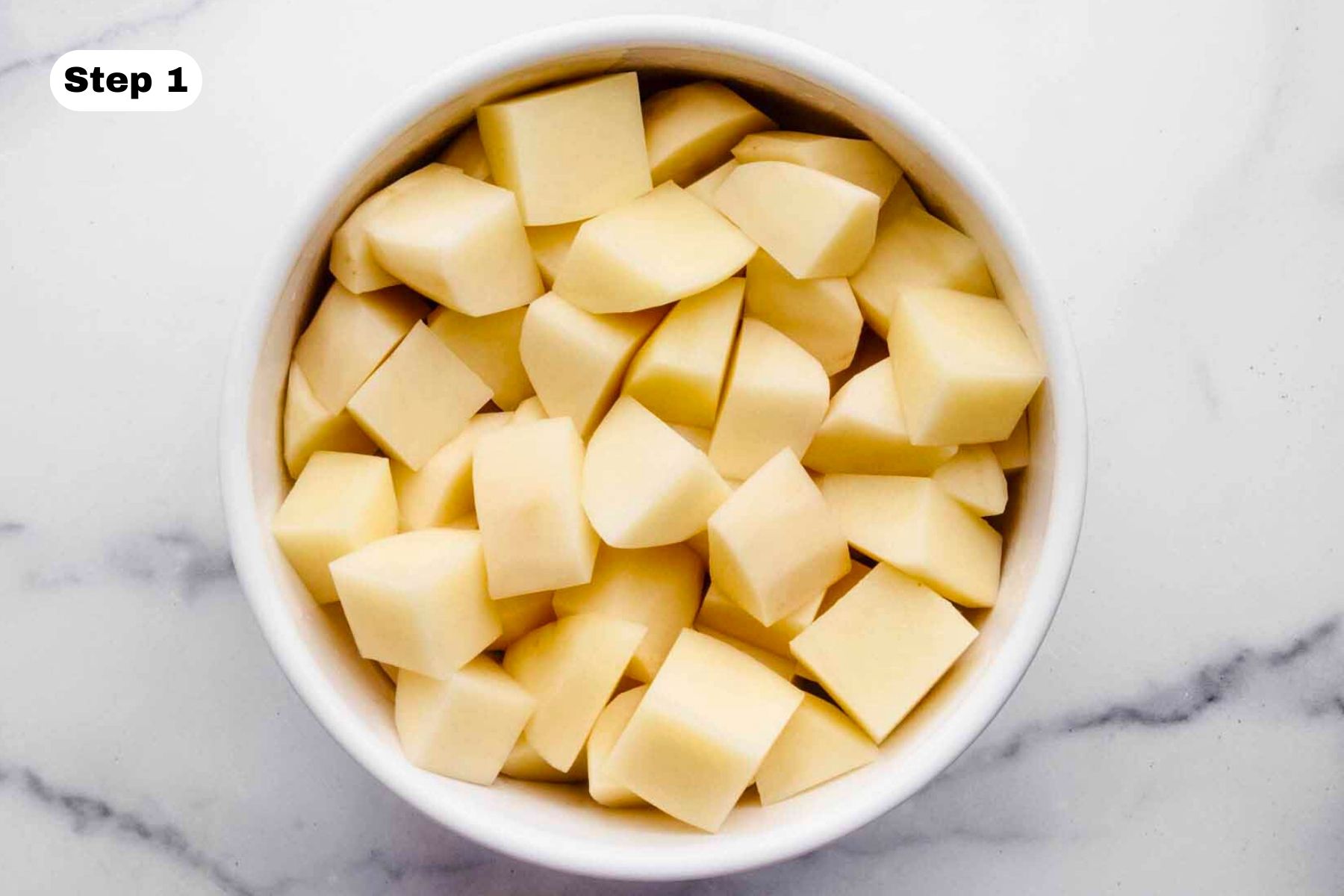Peeled and cubed potatoes in a white bowl.