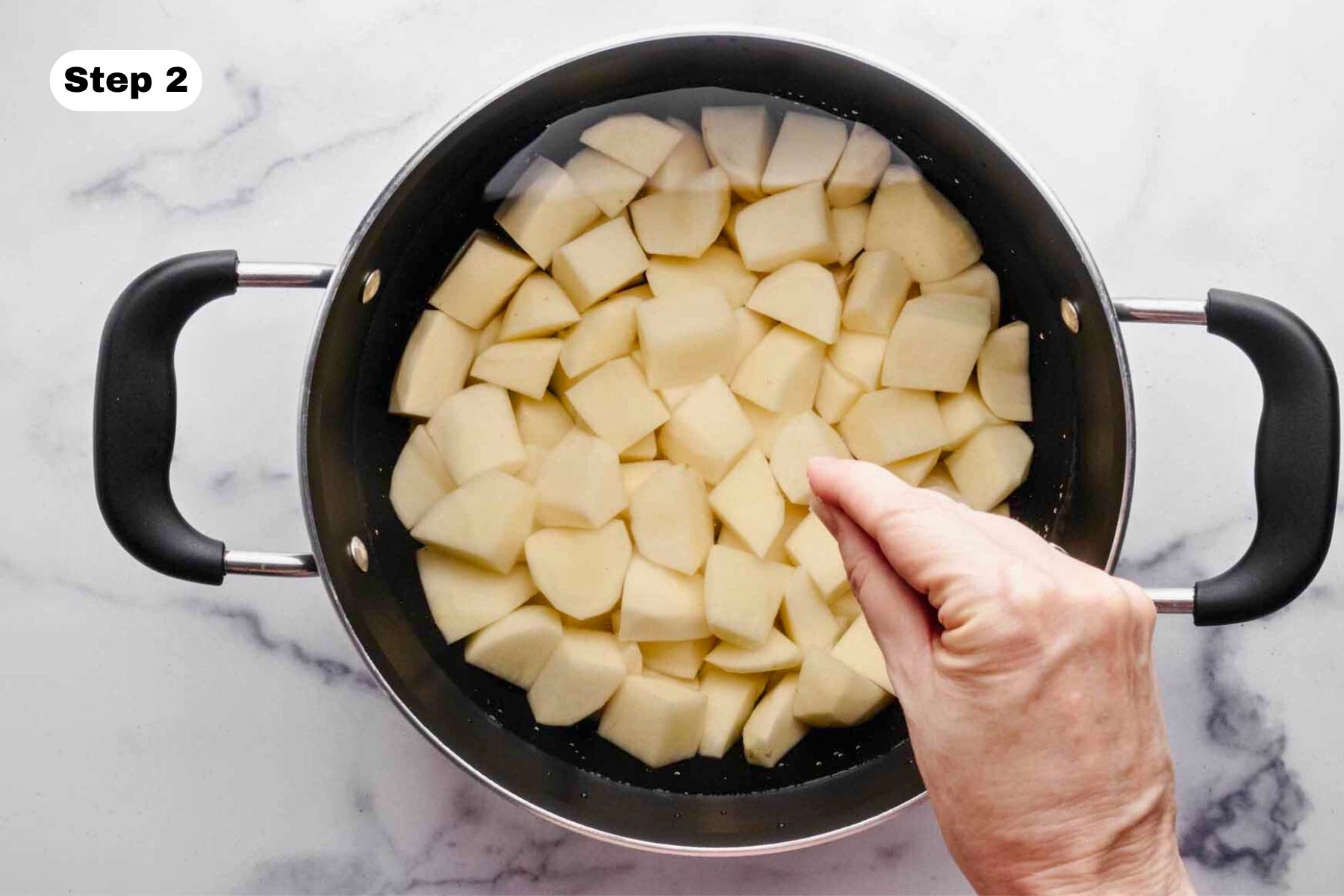 Potatoes covered with cold water in a large pot. A pinch of salt is being sprinkled over the top.