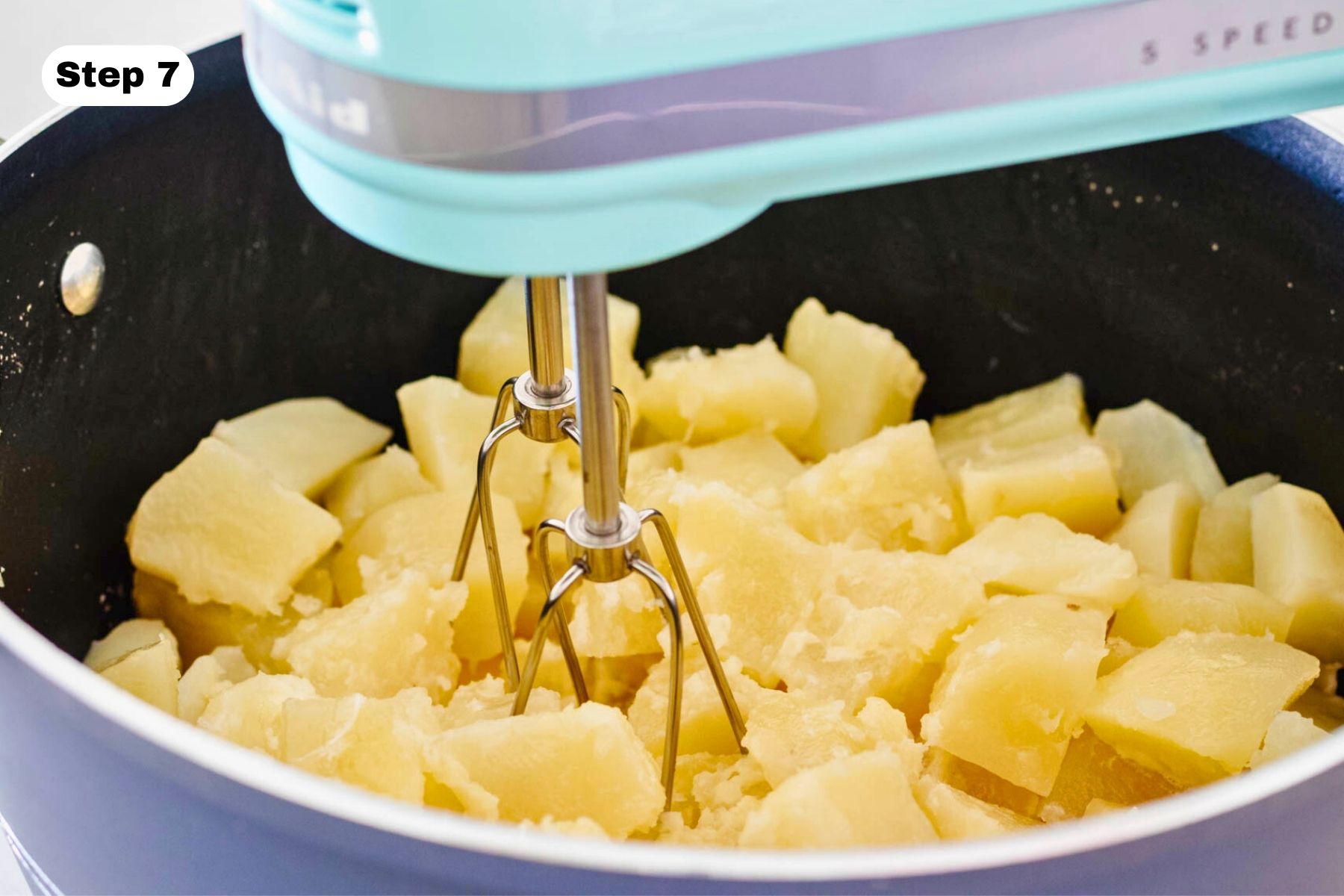 Potato mixture being whipped with a hand mixer in a large pot.