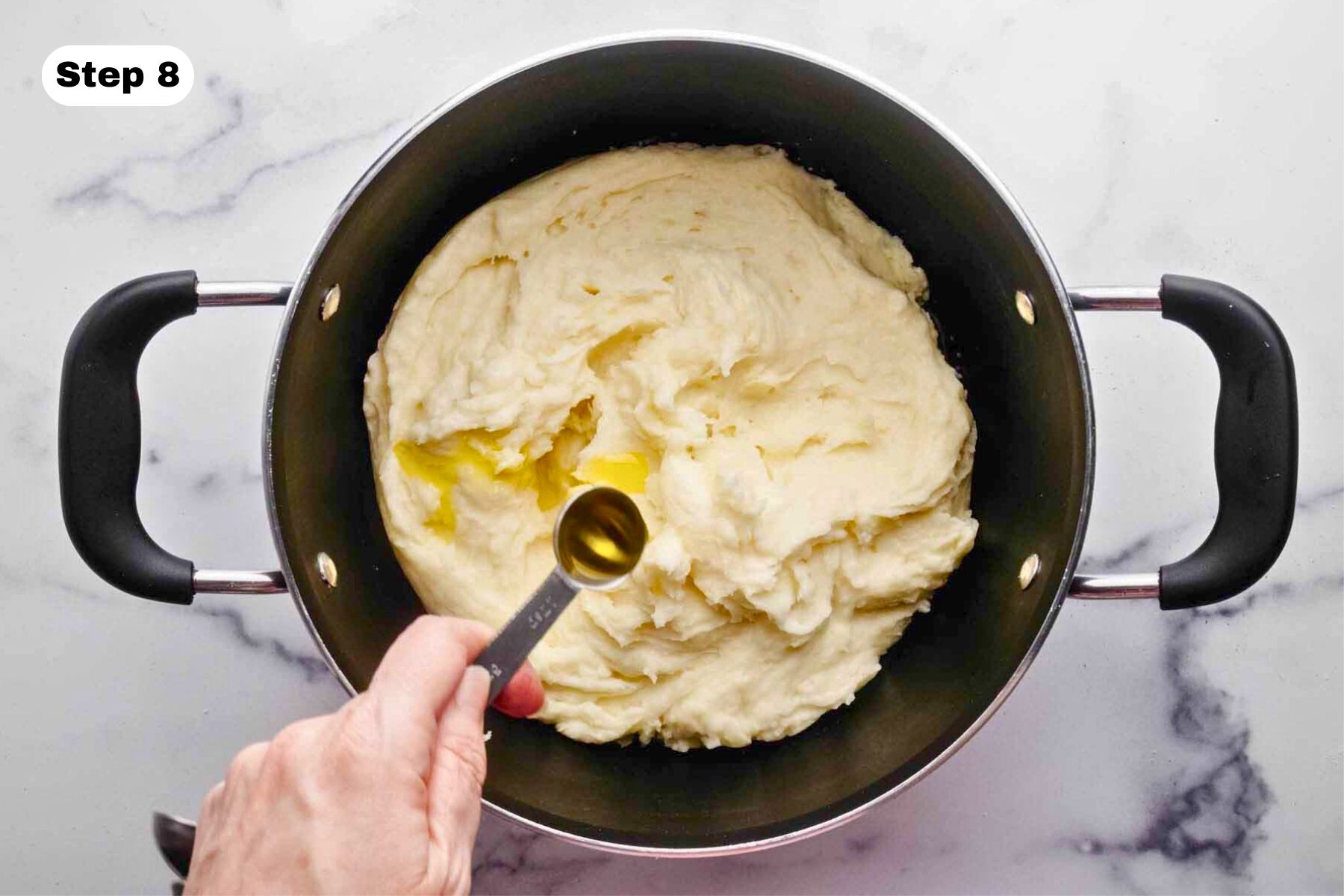 Truffle oil being added to mashed potatoes in a large pot.
