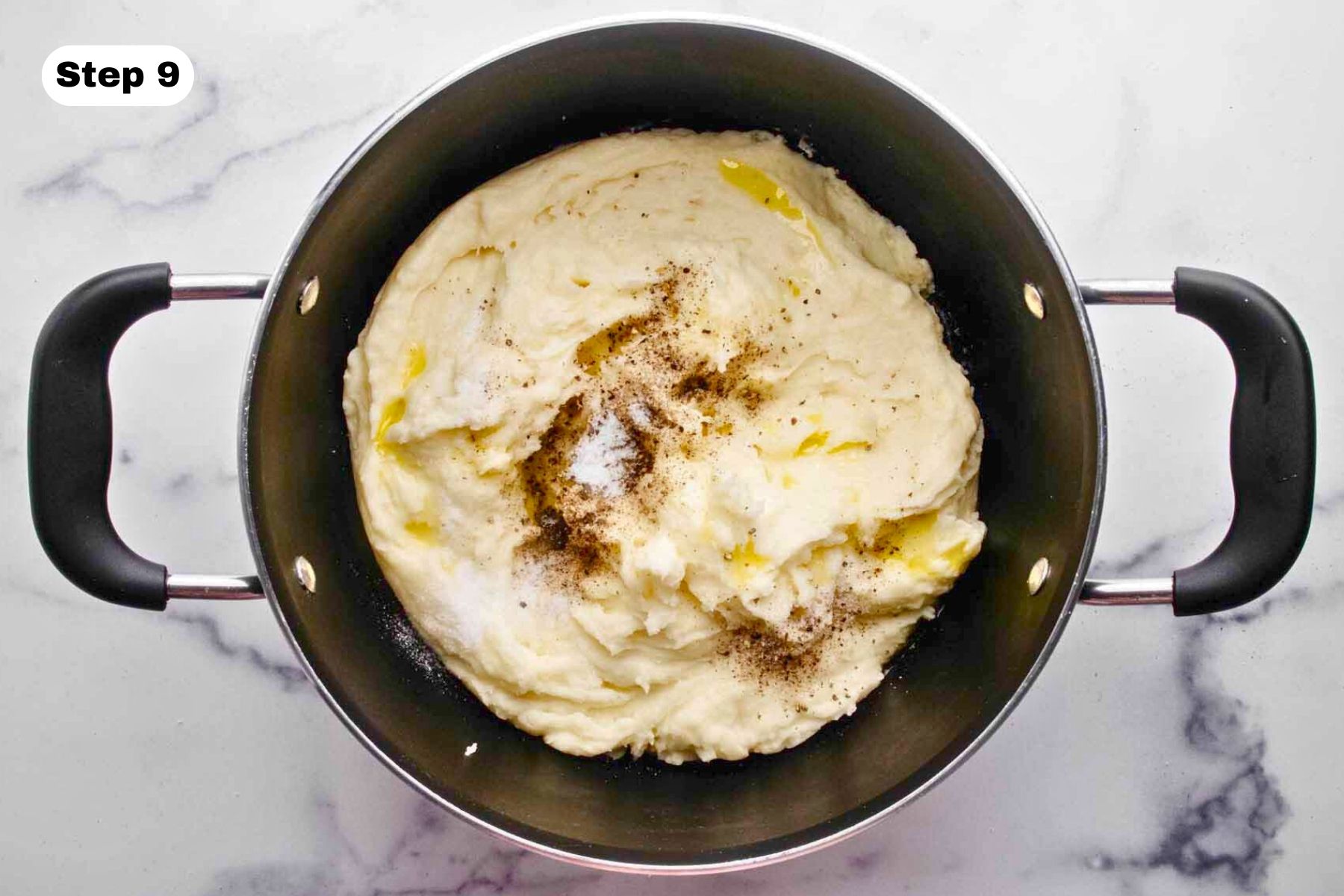 Salt and pepper sprinkled over the top of mashed potatoes in a large pot.