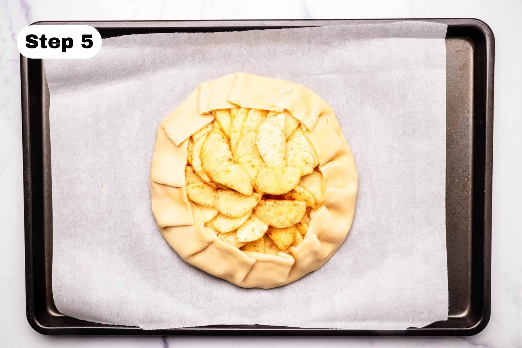 Unbaked apple galette on a baking sheet lined with parchment paper