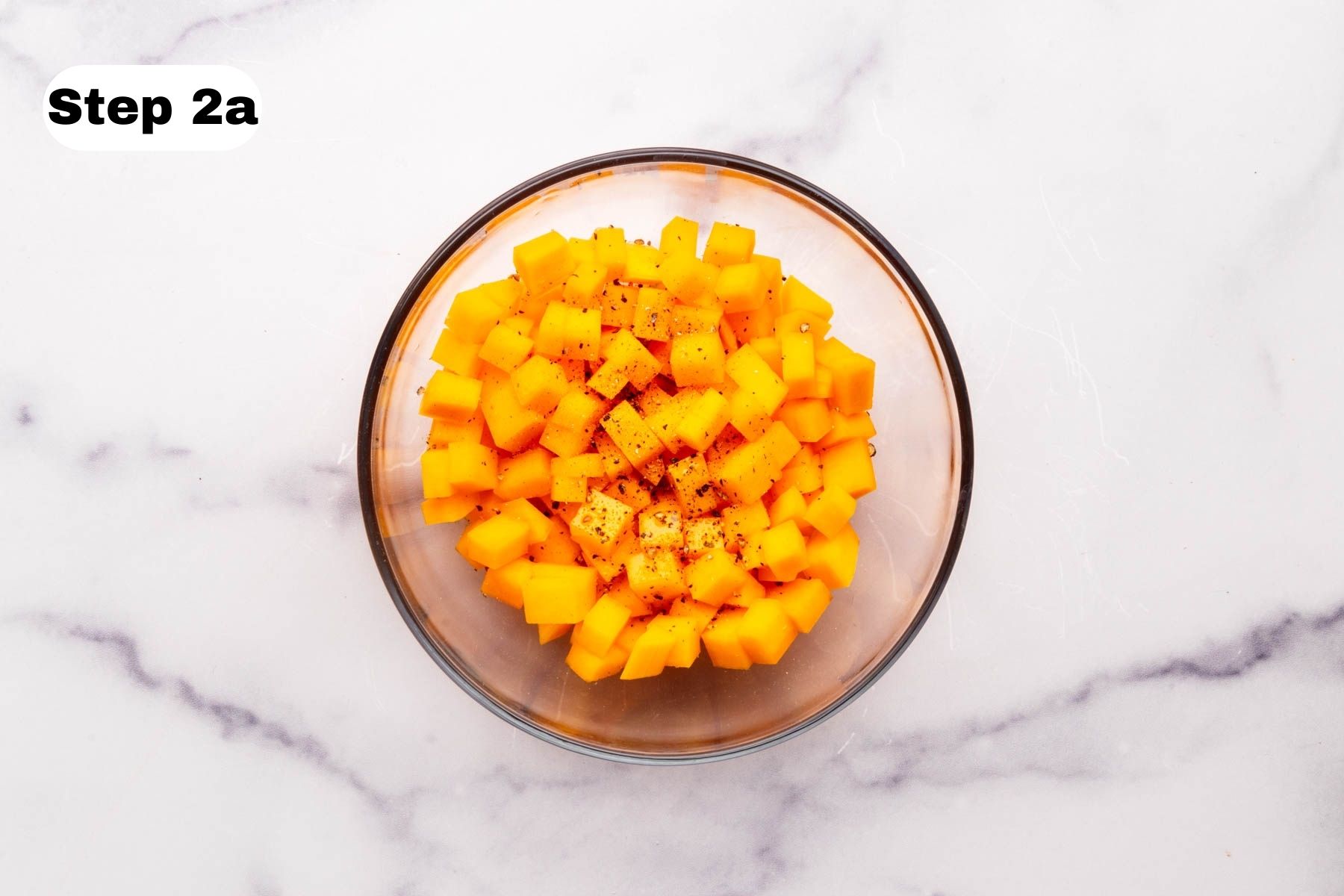 Diced butternut squash in a small glass bowl with olive oil, salt, and pepper
