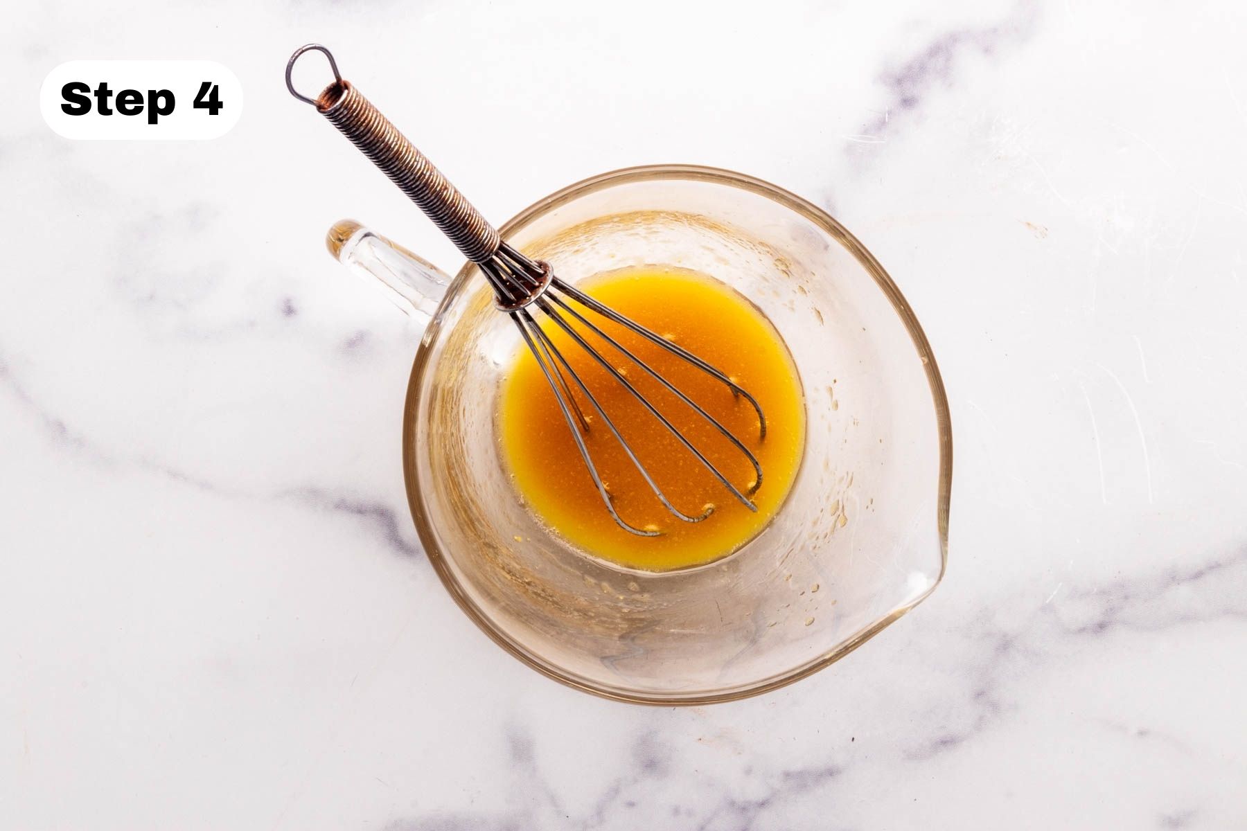 Dressing ingredients in a small glass pitcher with a small wire whisk