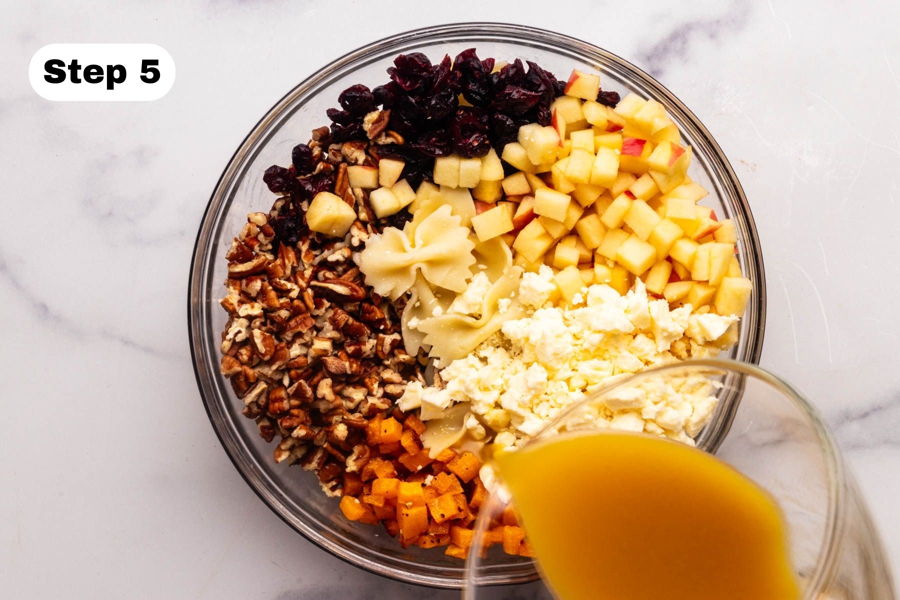 Dressing being poured over ingredients in a glass bowl