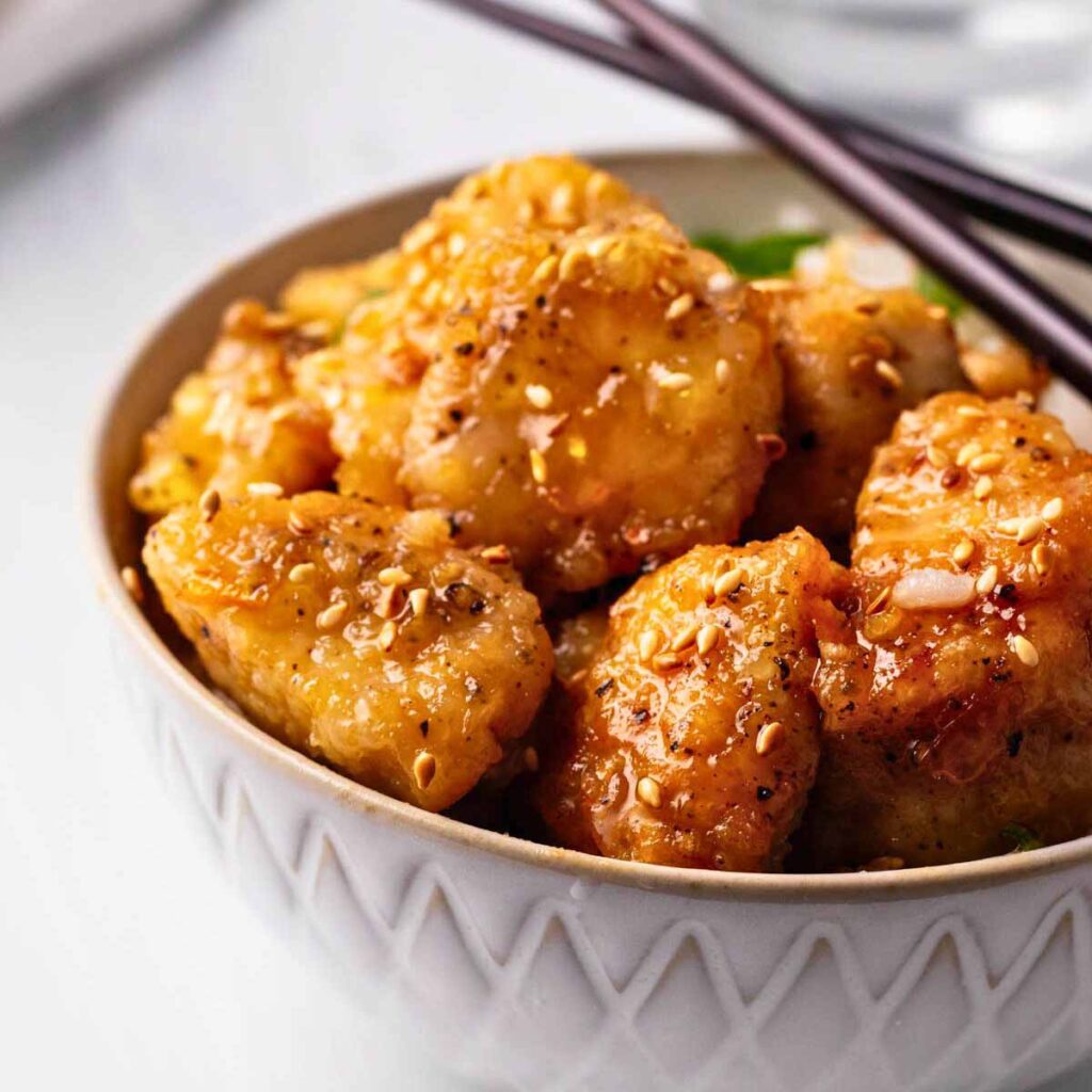 Close up of a bowl of orange chicken over rice with chopsticks