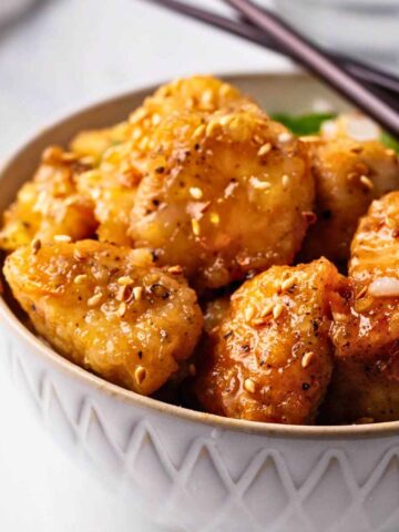 Close up of a bowl of orange chicken over rice with chopsticks