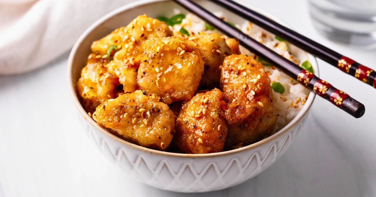 Close up of orange chicken in a small white bowl with chopsticks.