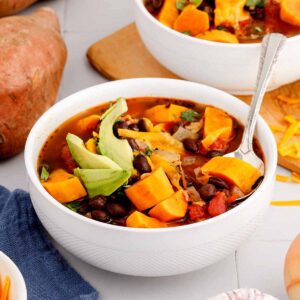 Close up of a serving of sweet potato black bean soup in a white bowl with a spoon