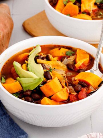Close up of a serving of sweet potato black bean soup in a white bowl with a spoon