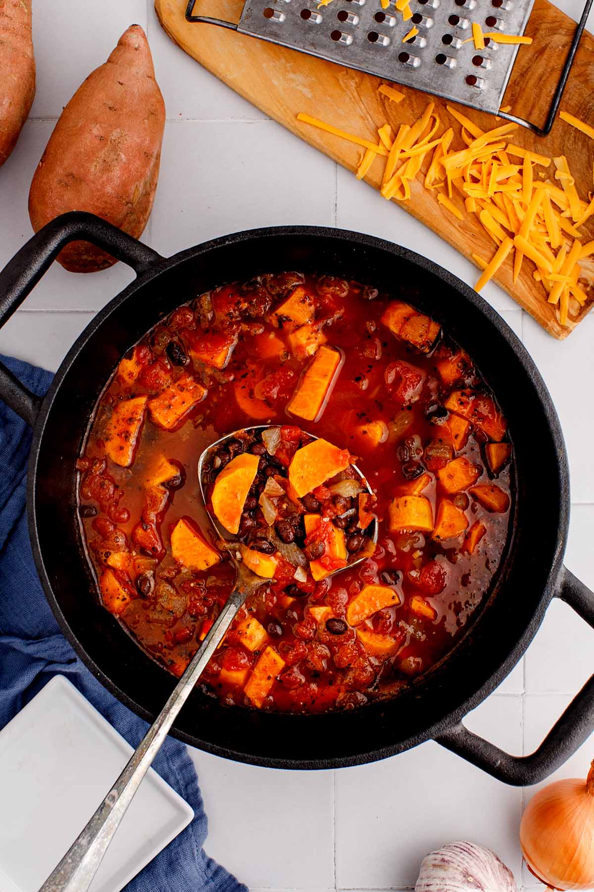 Overhead close up of sweet potato black bean soup in a soup pot with a ladle scooping out a serving