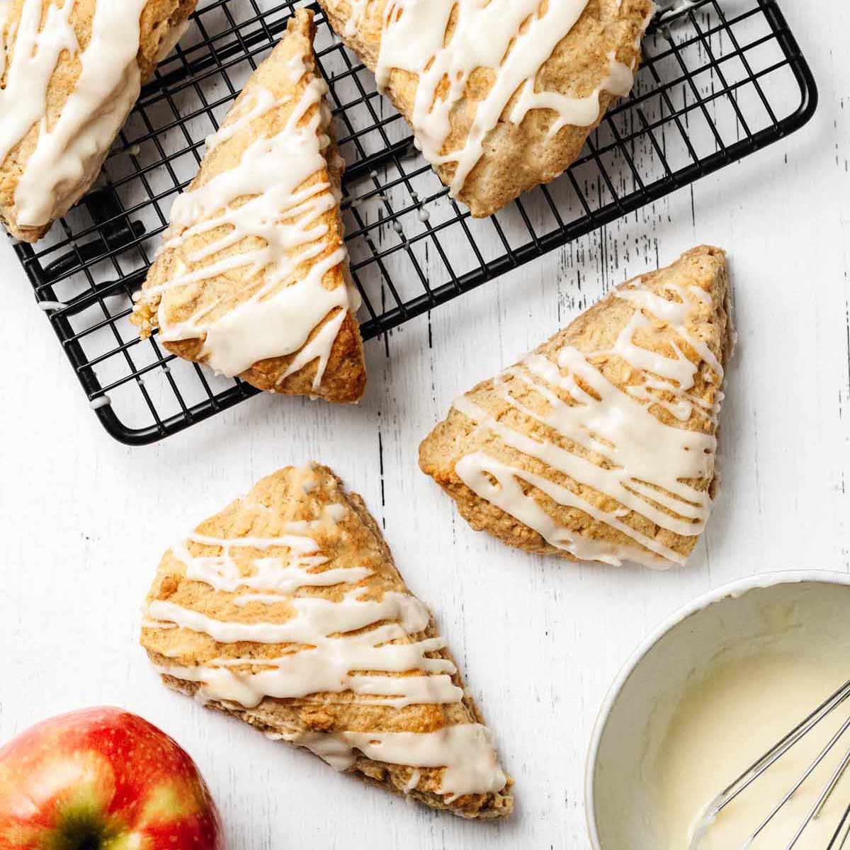 Overhead view of glazed apple scones on a white wooden surface and cooling on a wire rack.