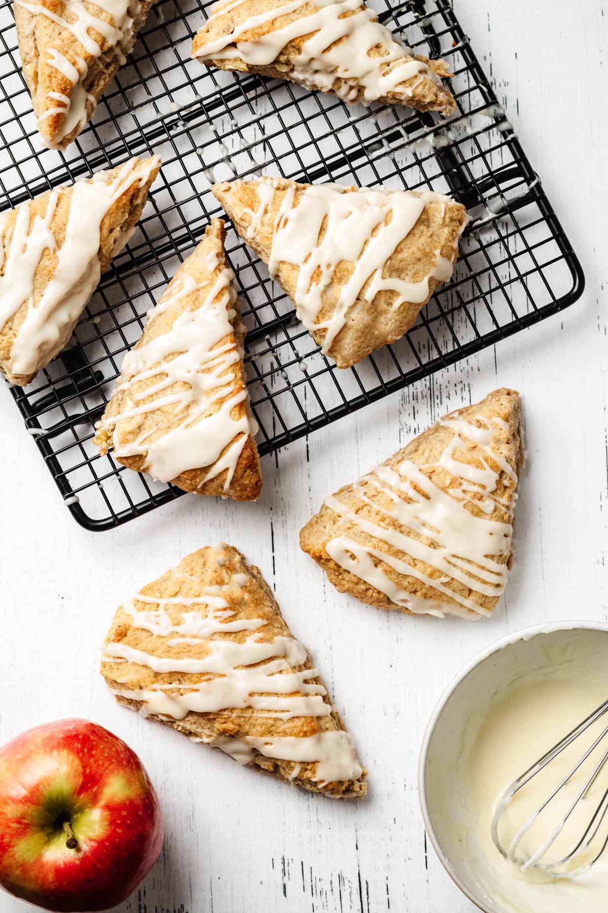 Overhead view of glazed apple scones on a white wooden surface and cooling on a wire rack.