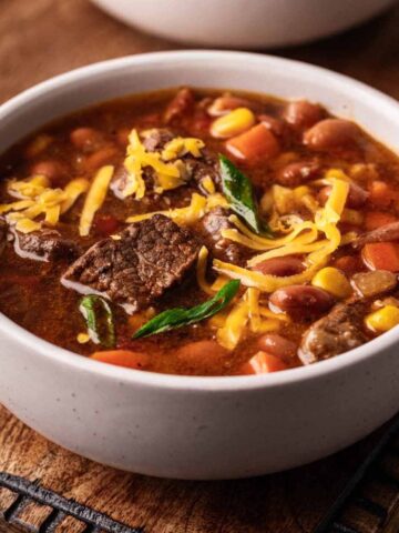Cowboy soup garnished with shredded cheddar cheese and sliced green onions in a large soup mug