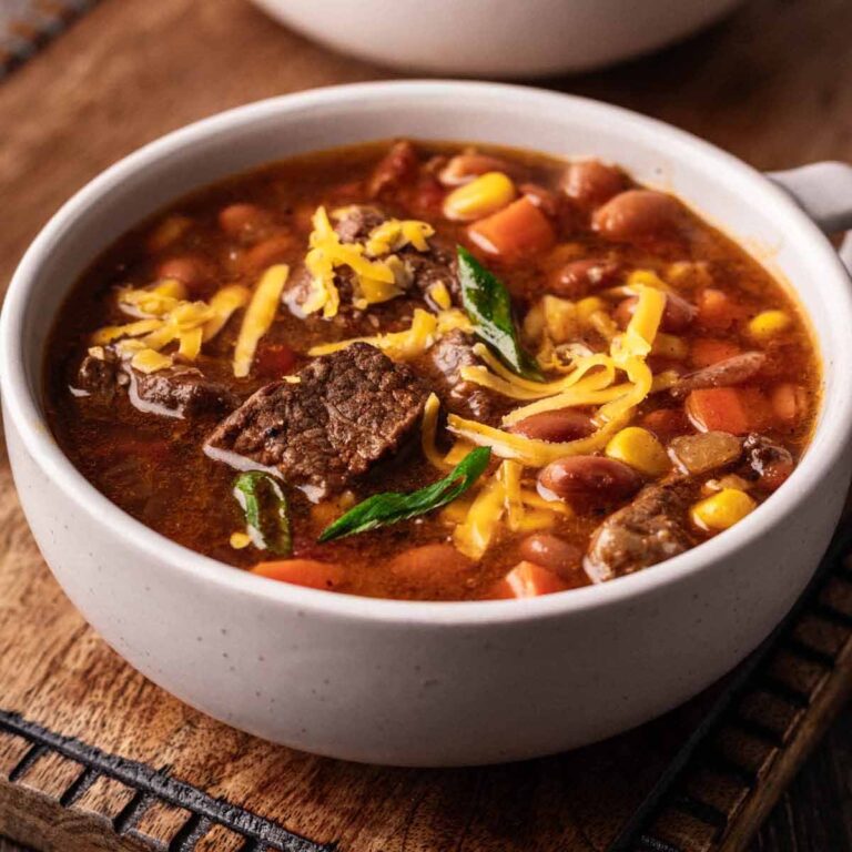 Cowboy soup garnished with shredded cheddar cheese and sliced green onions in a large soup mug