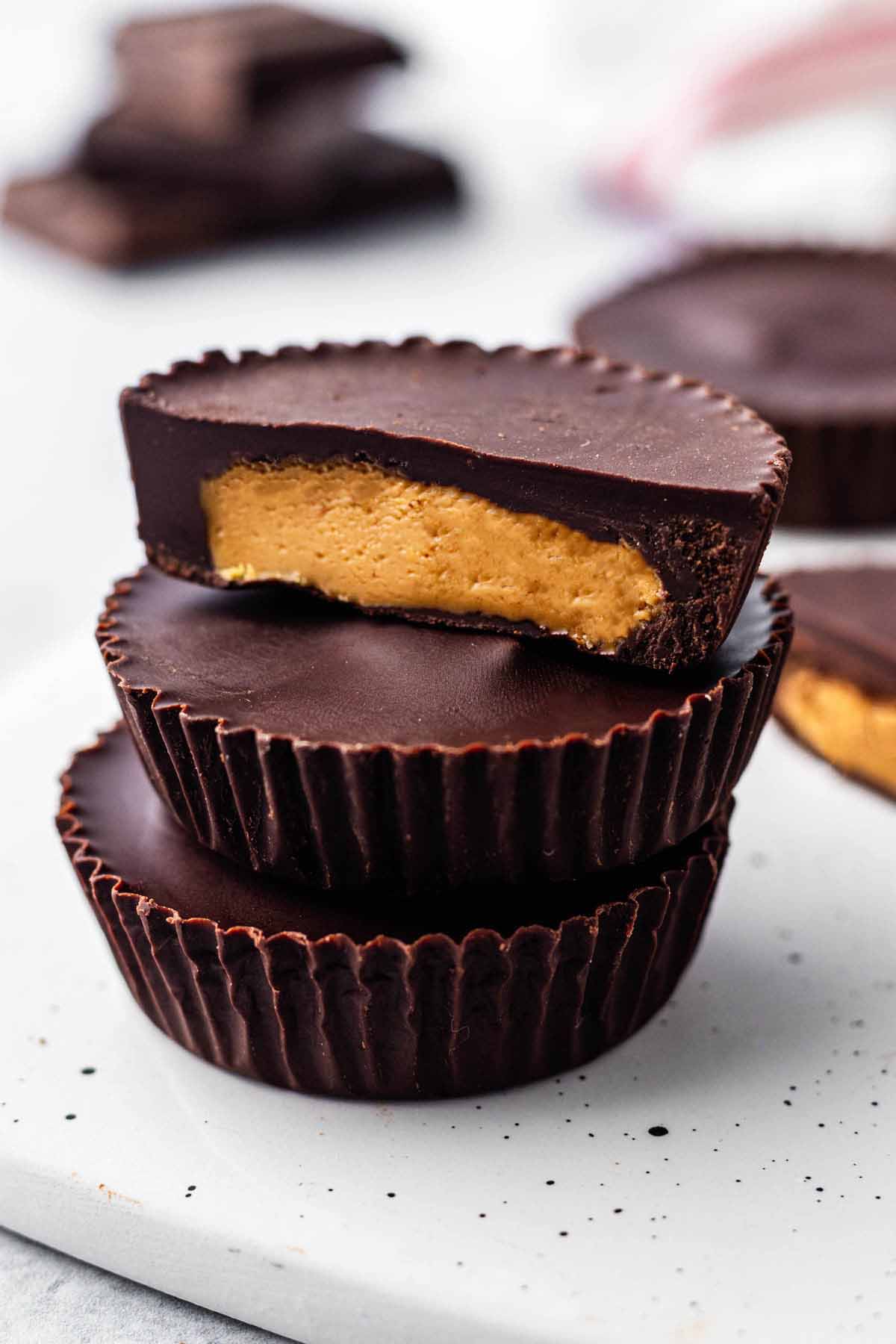 Three peanut butter cups stacked on a white surface. The top cup is cut in half to expose the creamy filling.