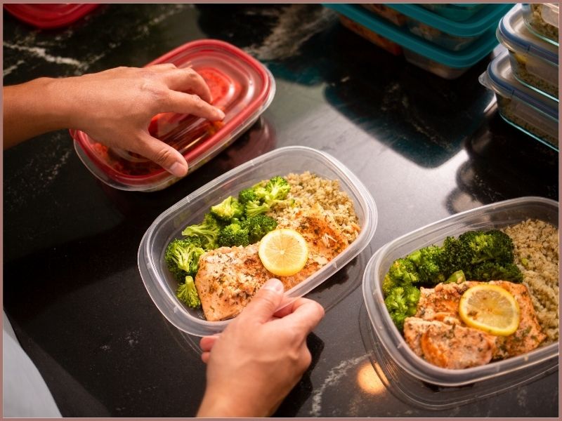 Man preparing a meals of salmon, rice and broccoli in plastic meal prep containers.