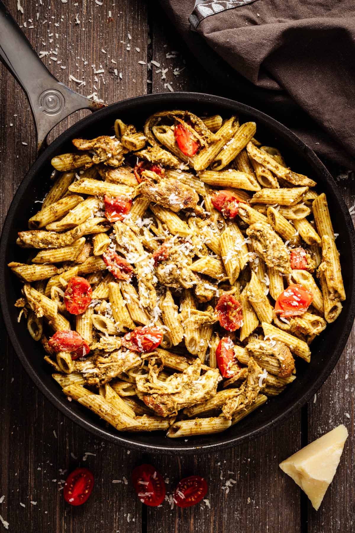 Overhead view of pesto chicken pasta garnished with grated Parmesan cheese in a dark skillet