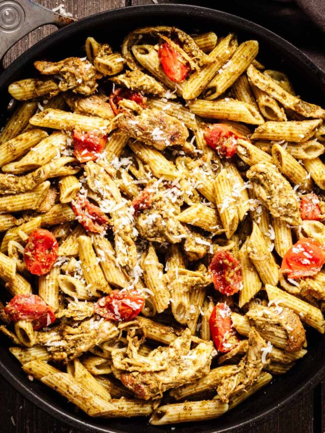 Overhead view of pesto chicken pasta garnished with grated Parmesan cheese in a dark skillet