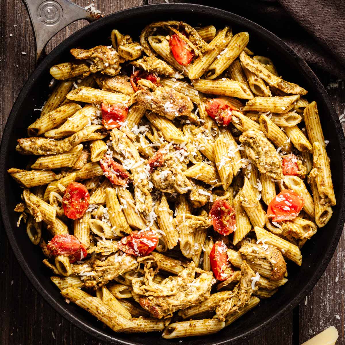 Overhead view of pesto chicken pasta garnished with grated Parmesan cheese in a dark skillet