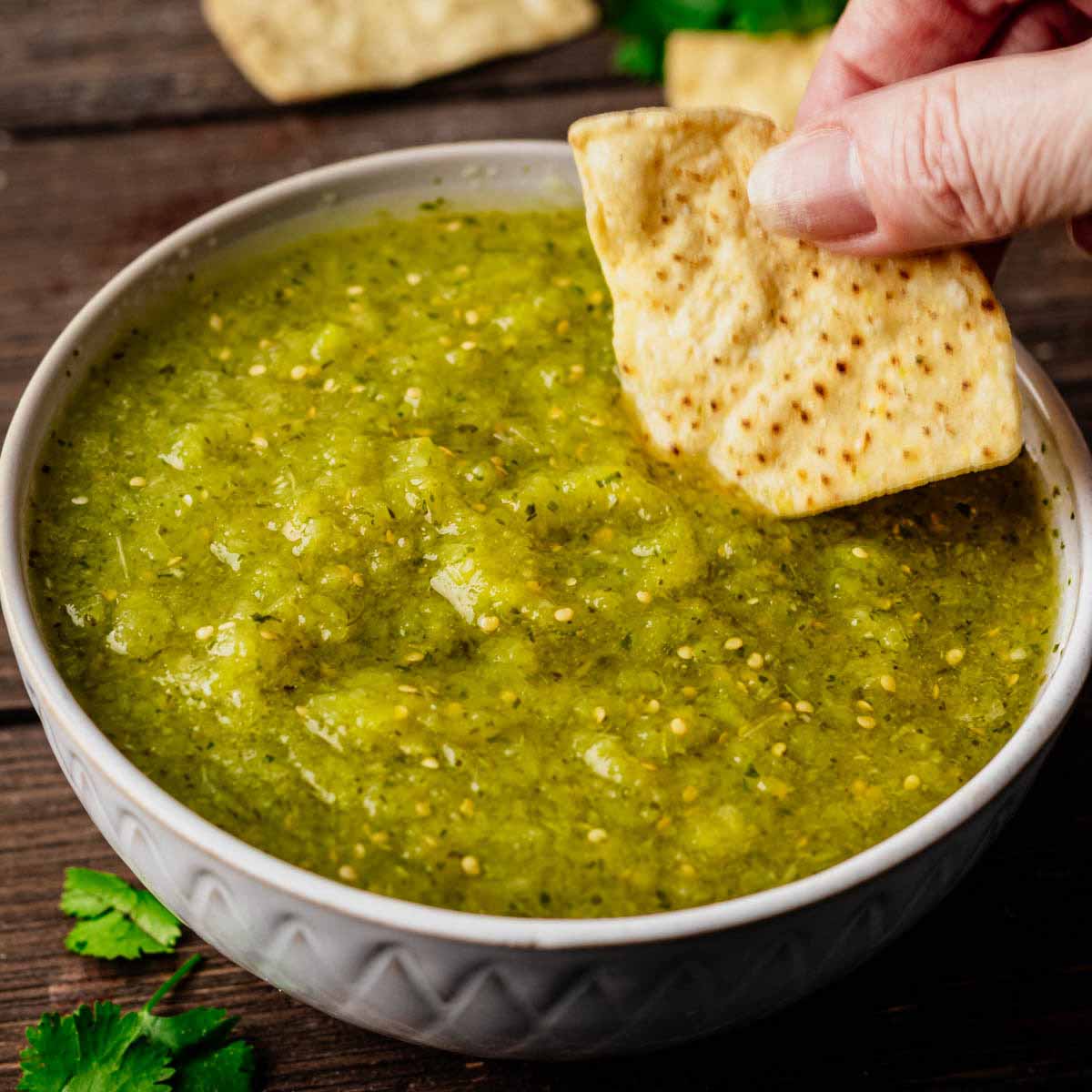 Tomatillo salsa in a small grey bowl with a tortilla chip being dipped into it.