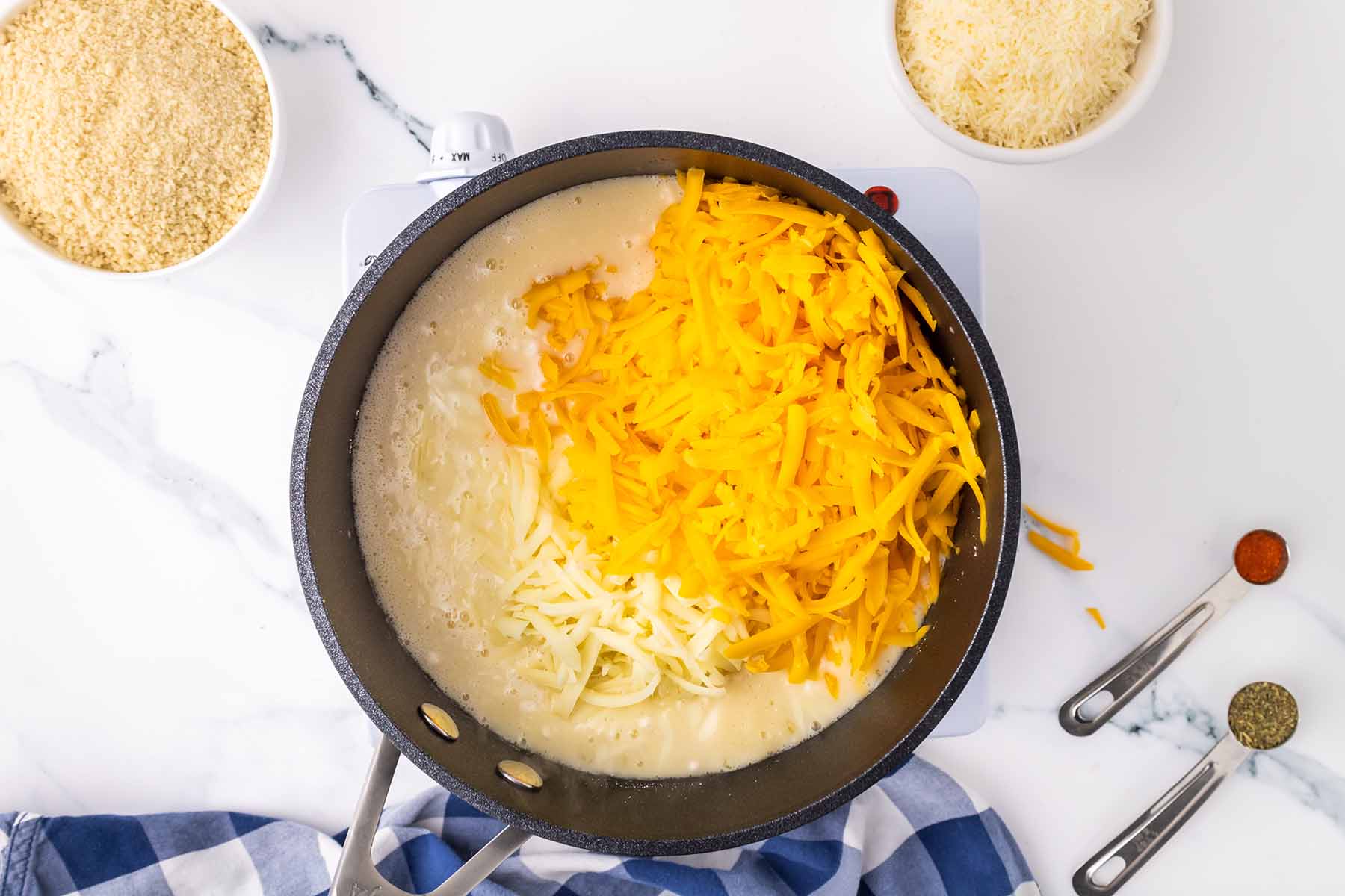 Shredded cheddar and mozzarella cheese added to a creamy sauce in a saucepan, preparing the cheese sauce for baked macaroni and cheese.