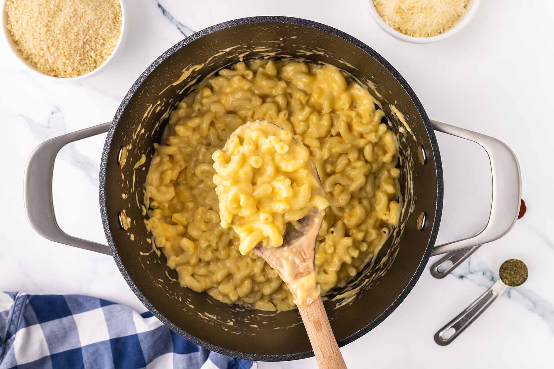 Creamy macaroni and cheese being stirred in a large pot with a wooden spoon, ready to be transferred to a baking dish.