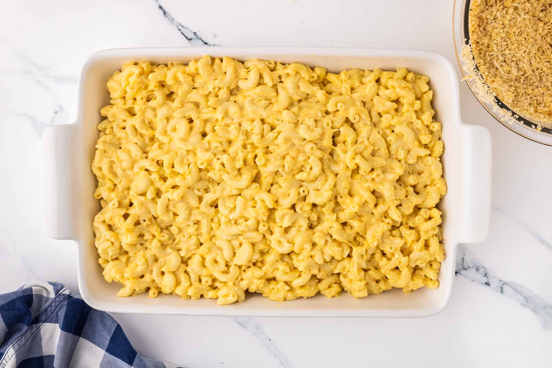 Creamy macaroni and cheese spread evenly in a white baking dish, ready for the breadcrumb topping.