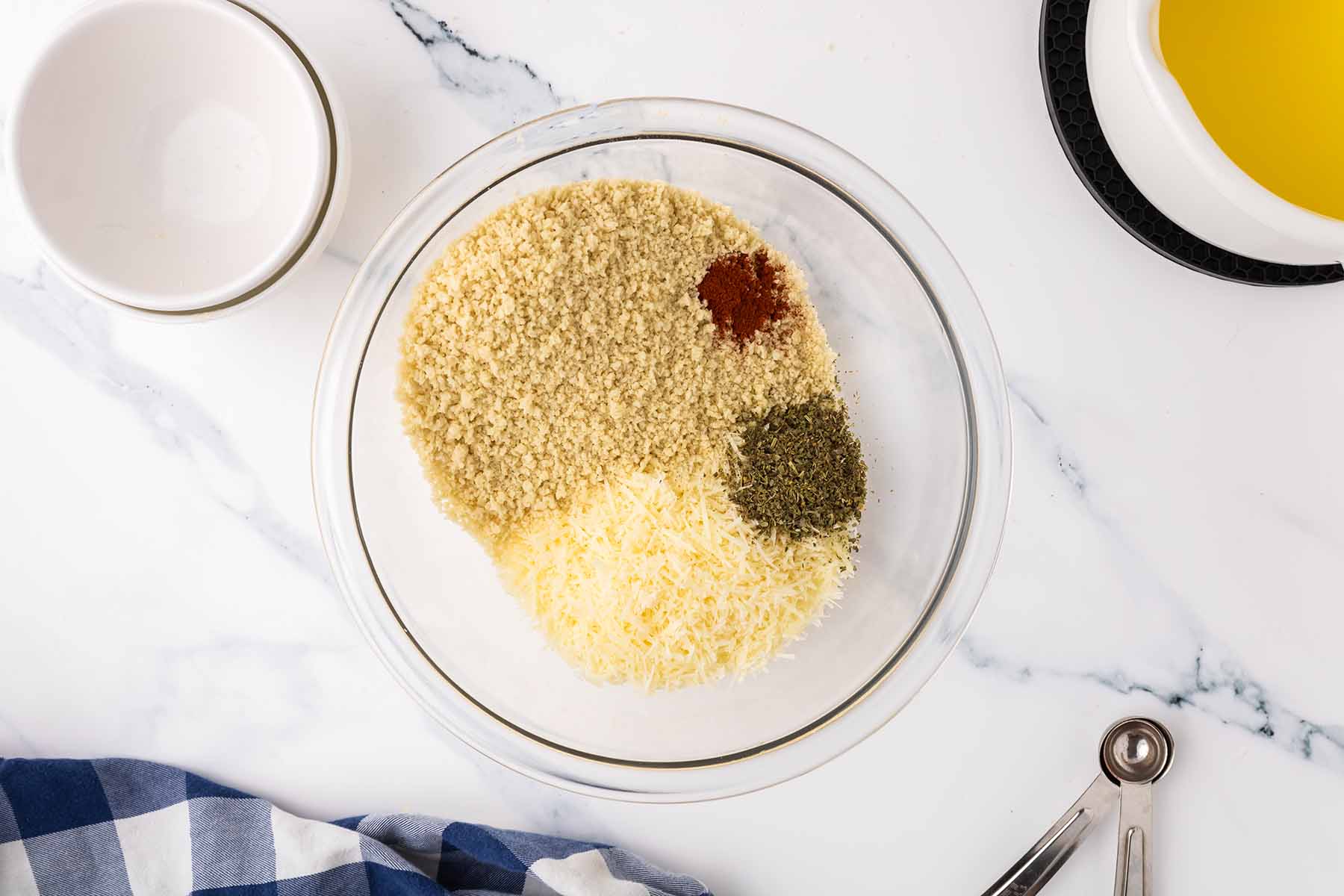 A glass bowl with breadcrumbs, grated parmesan, paprika, and dried herbs, ready to be mixed for the topping of baked macaroni and cheese.