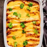 Baked beef and bean enchiladas in a white dish, topped with melted cheddar cheese and fresh cilantro garnish.