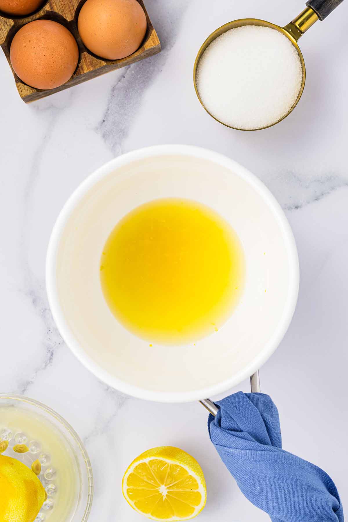 Bowl of lemon juice and zest over a pot, with eggs, sugar, and a juiced lemon nearby. Step 1 of making lemon curd for lemon mousse.