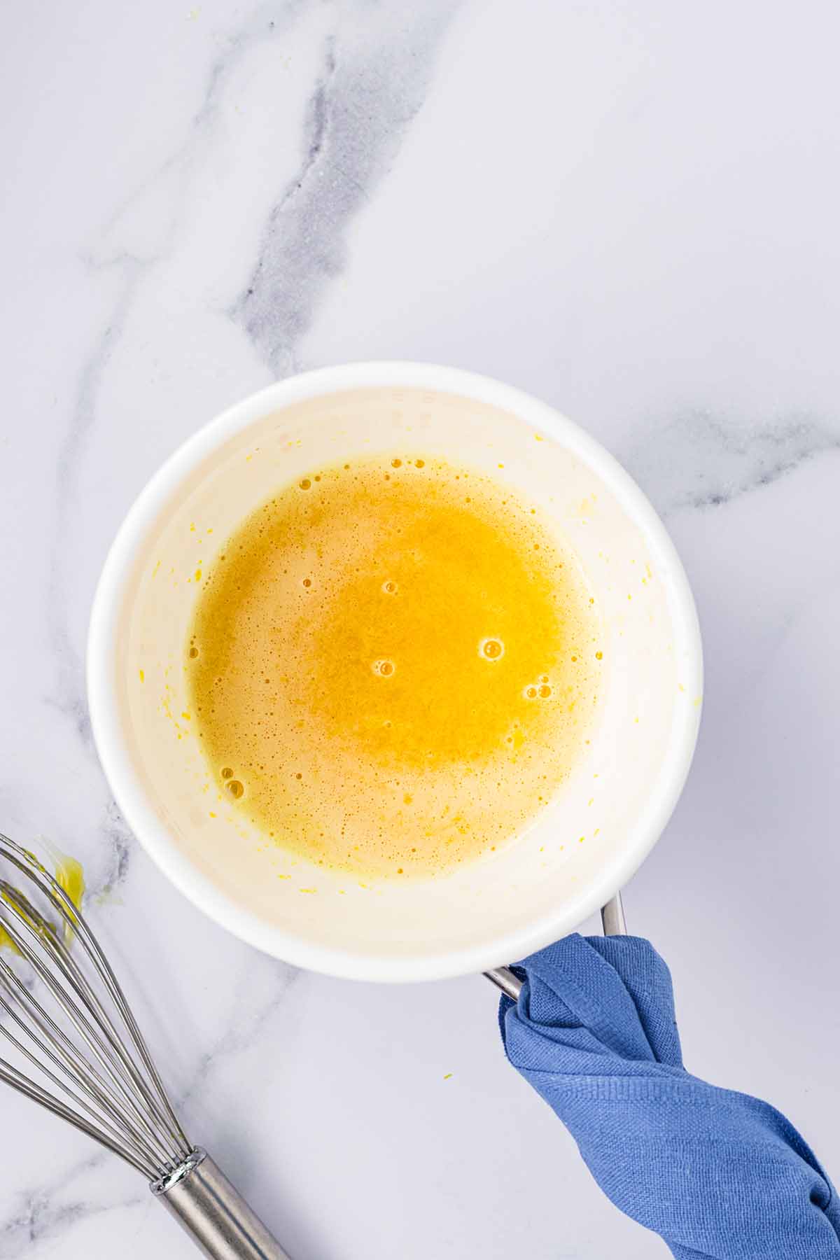 Whisked lemon curd mixture in a bowl over a pot with a whisk next to it. Step 3 of making lemon curd for lemon mousse.