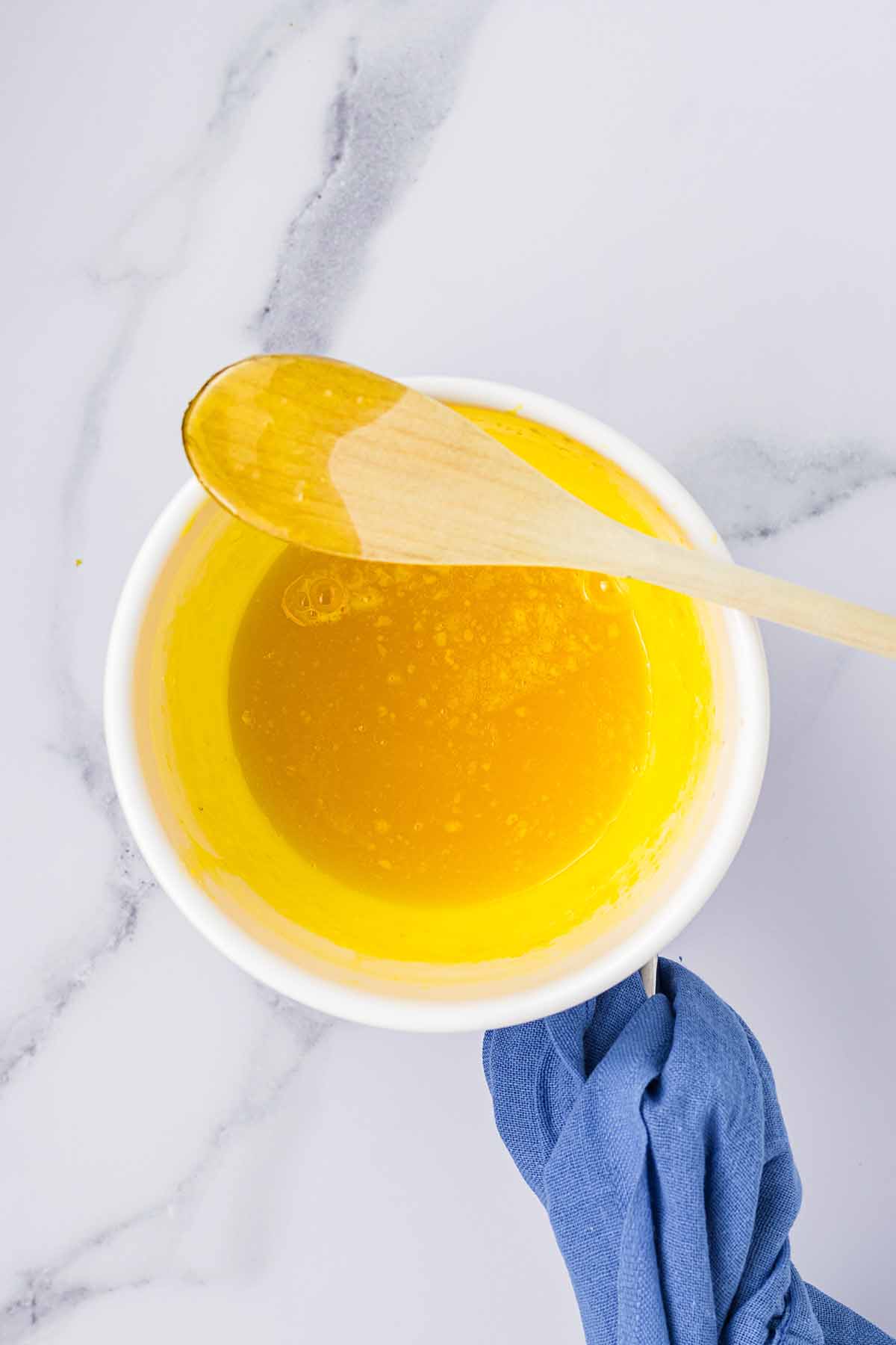 Lemon curd thickening in a bowl with a wooden spoon resting on top. Step 4 of making lemon curd for lemon mousse.