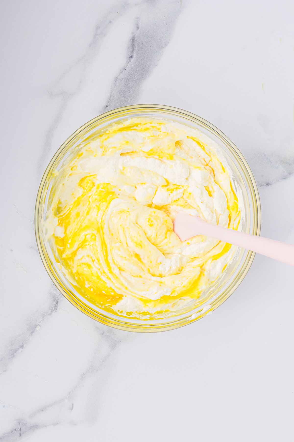 Lemon curd being folded into whipped cream in a bowl. Step 7 of making lemon mousse.