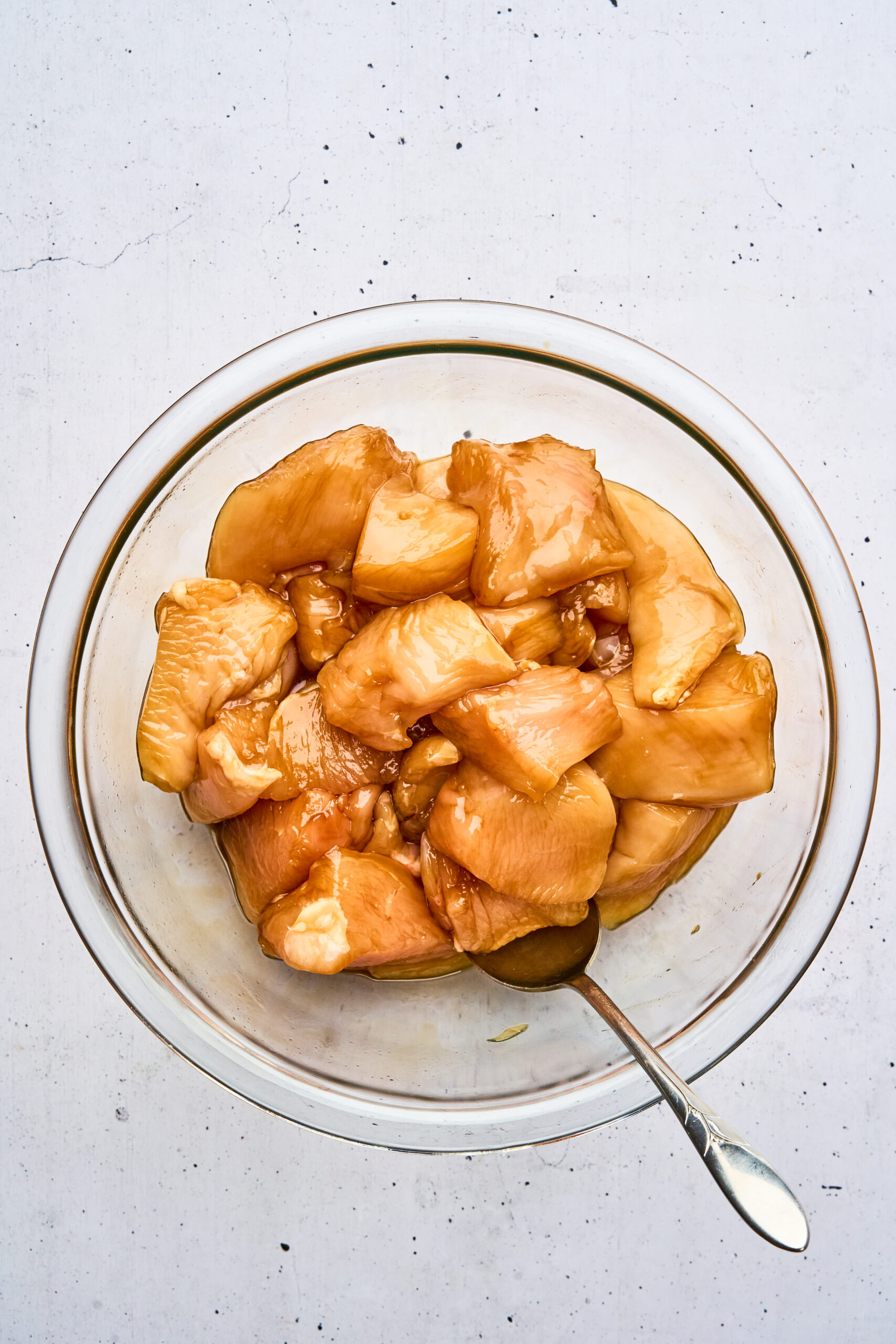 Overhead view of raw chicken pieces marinating in a bowl with a spoon.