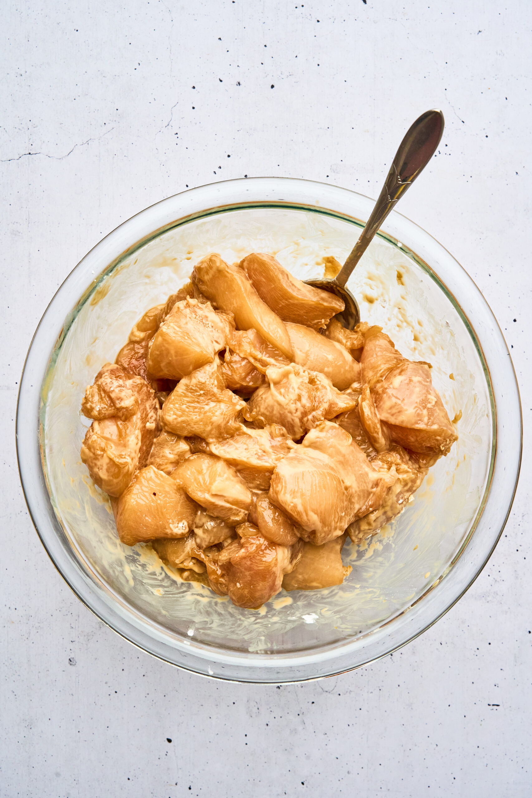 Overhead view of raw chicken pieces coated in a marinade and cornstarch in a bowl, with a spoon.