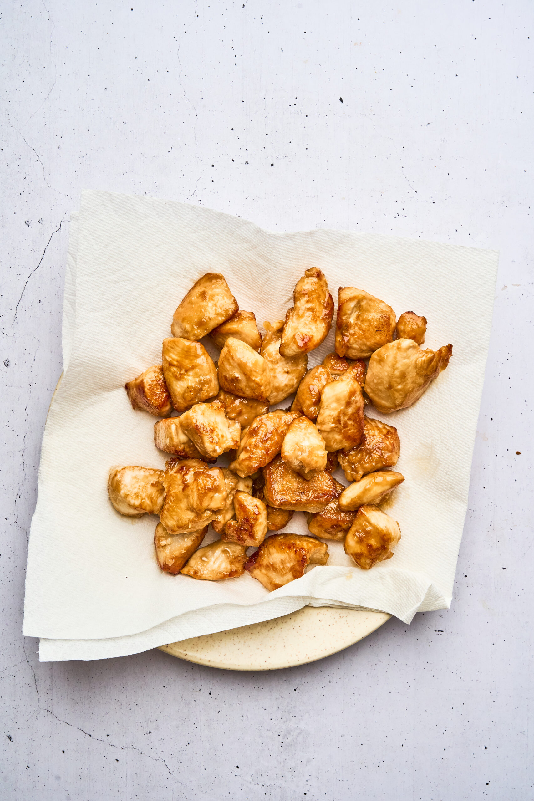 Overhead view of cooked chicken pieces resting on a paper towel-lined plate to drain excess oil.