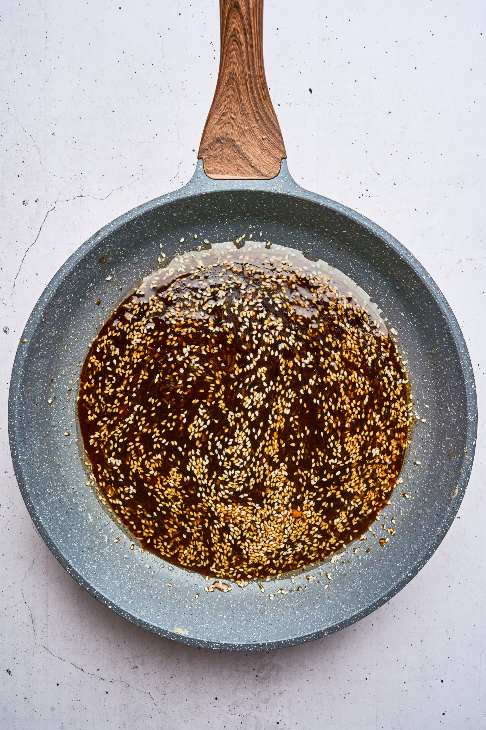 Overhead view of sesame seeds and sauce simmering in a frying pan.