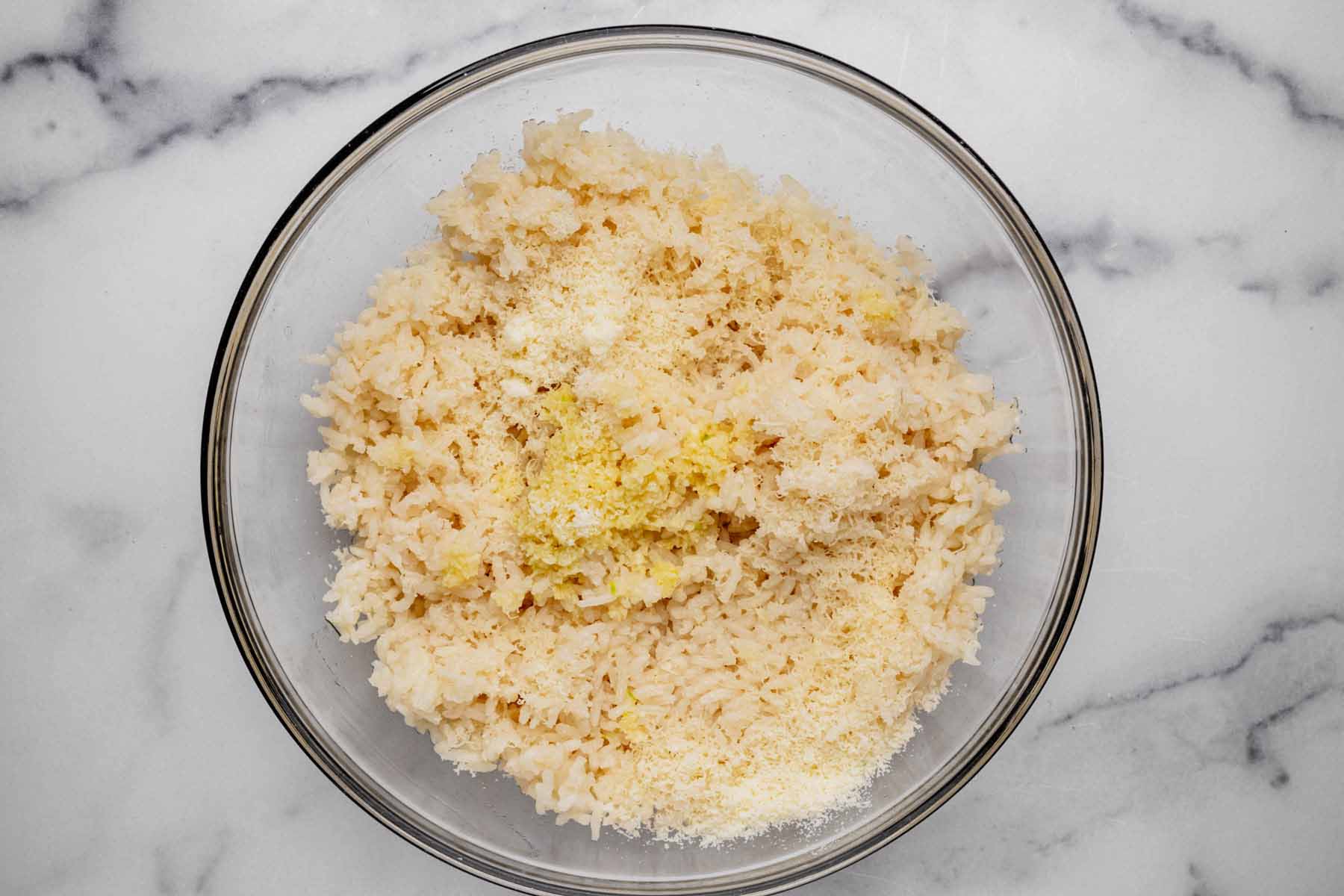 Cooked rice in a glass bowl mixed with freshly sautéed garlic, melted butter, and grated Parmesan cheese, ready to be combined for Garlic Parmesan Rice.