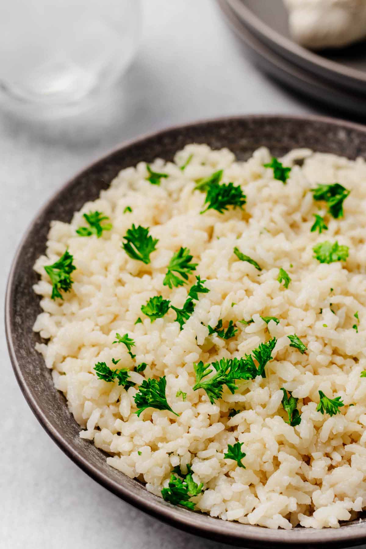 Garlic Parmesan Rice in a dark bowl, garnished with fresh parsley, served on a light background with subtle tableware in the backdrop.