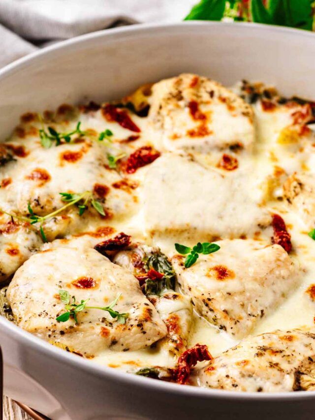 Close-up of a creamy Tuscan chicken bake topped with melted mozzarella cheese, sun-dried tomatoes, and fresh herbs in a white baking dish.