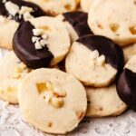 Close-up of Hawaiian shortbread cookies featuring macadamia nuts and dried pineapple, with some cookies partially dipped in dark chocolate and garnished with chopped nuts.
