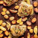 Golden roasted chicken thighs and potatoes on a dark baking sheet, drizzled with honey mustard sauce and garnished with fresh thyme sprigs.