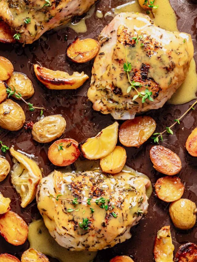 Golden roasted chicken thighs and potatoes on a dark baking sheet, drizzled with honey mustard sauce and garnished with fresh thyme sprigs.